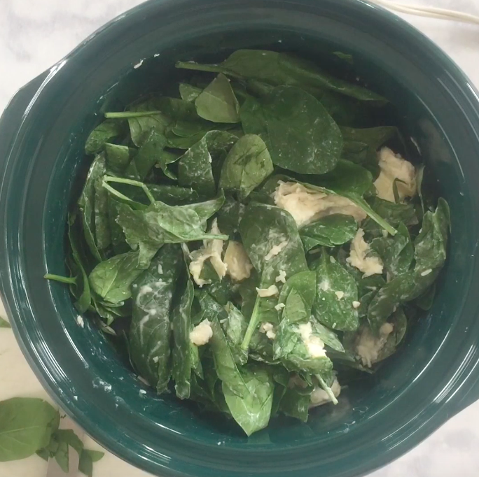 spinach and dip in a green crockpot ready to be cooked