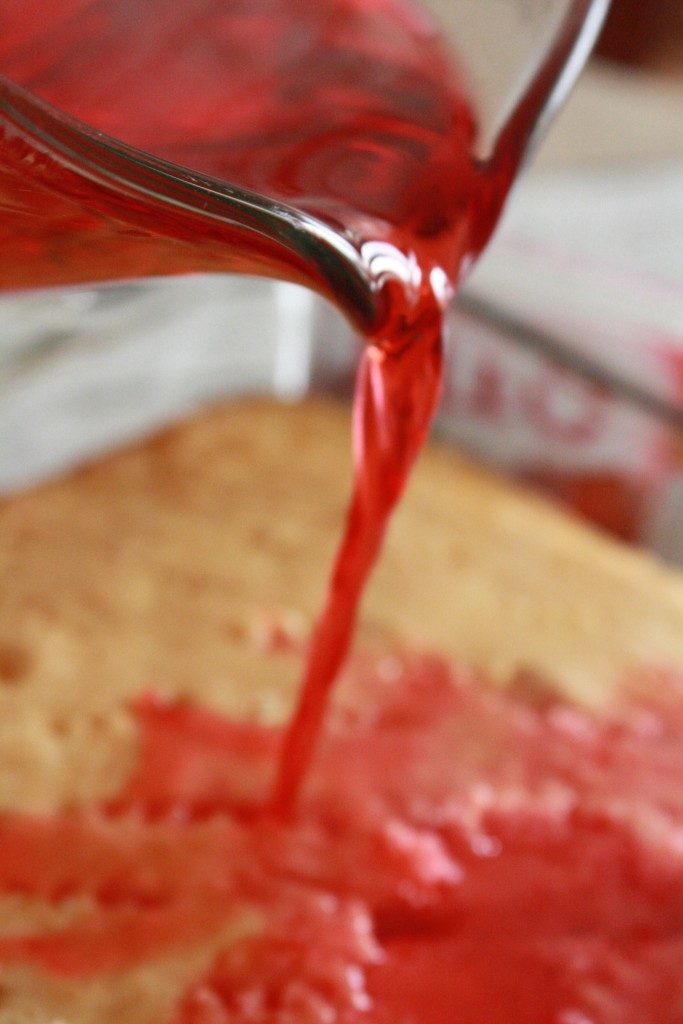 Pouring strawberry jello liquid over poke cake holes