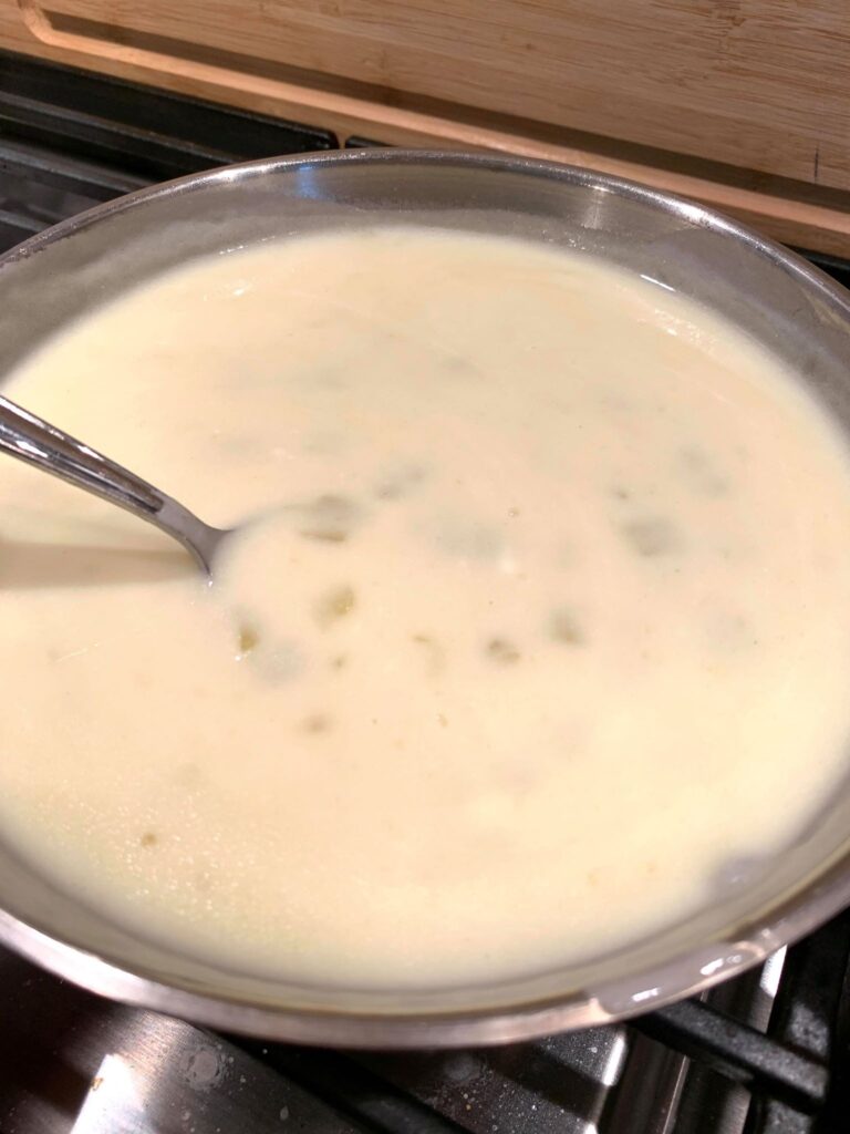 white enchilada sauce with green chilies in a pan ready to go over white chicken enchiladas